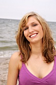 Portrait of beautiful woman wearing purple top standing on beach, smiling