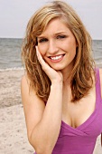 Portrait of beautiful blonde woman wearing pink top standing on beach, smiling