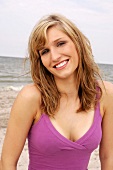 Portrait of beautiful blonde woman wearing pink top standing on beach, smiling