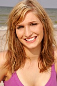 Portrait of beautiful blonde woman wearing pink top standing on beach, smiling