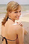 Close-up of attractive blonde woman sitting on beach and applying cream on back