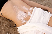 Close-up of woman lying on sand with salt crystals on belly