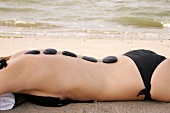 Rear view of blonde woman lying on beach with stones on her back