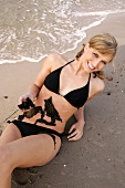 Portrait of pretty woman in black bikini lying on beach with seaweed on her belly, smiling