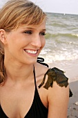 Portrait of beautiful woman in black bikini top sitting with seaweed on shoulder, smiling