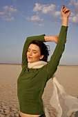 Carefree woman in green sweater, jeans and scarf enjoying sun on beach
