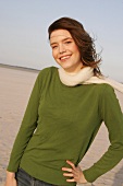 Beautiful woman wearing green sweater, jeans and scarf, standing and smiling