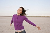 Pretty woman wearing purple sweater standing on beach, smiling with eyes closed
