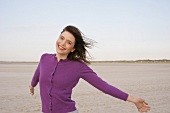 Pretty woman wearing purple sweater standing on beach, smiling with eyes closed