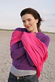 Portrait of pretty woman wearing purple sweater and pink shawl standing on beach, smiling