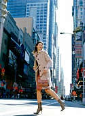 Frau im Mantel, Rock + hochhackigen Stiefeletten geht fröhlich in NY