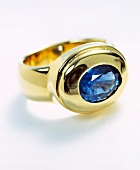 Close-up of golden ring with blue precious stone on white background