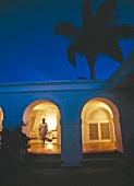 Maid walking out of illuminated bedroom of villa at night