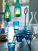 Lit lanterns, Ouzo in decanter bottle and iron frame with blue glasses on table