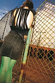 Rear view of sad woman wearing fringed top, mini skirt and stockings leaning on fence
