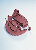 Close-up of crumbled pink silky shimmer blush on white background