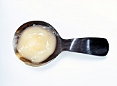 Close-up of orange flavoured dollop face mask in horn spoon on white background