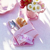 Besteck und Brötchen gewickelt in rosa Serviette, Band, Namensschild