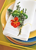 Kräutersträußchen mit Blume in Orange auf Serviette als Tischdeko