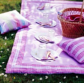 Purple picnic blanket with picnic basket, pillows and cutlery in garden