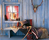 Sitzbank mit Kissen an Bretterwand in Blau, Fenster beleuchtet, Winter