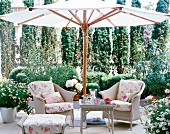 Wicker chair with floral patterned cushions under white parasol in garden