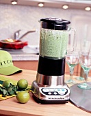 Mixer with limes and herbs on wooden table