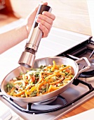 Woman spreading pepper in vegetable while cooking