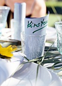 Namenskärtchen im Glas als Platz- halter auf gedecktem Tisch.