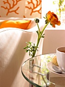 Orangene Blume, die neben einer Tasse Kaffee an einem Tisch steht.