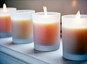 4 Kerzen in milchigen Gläsern stehen auf einer Fensterbank.