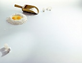 Egg yolk in flour, flour scoop and broken egg shells on white background