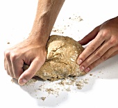 Hand kneading chestnut pasta dough on white background, step 3