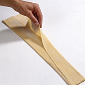 Hand folding pasta dough in three layer strip on white background