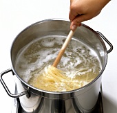 String noodles being stirred with wooden fork in pot