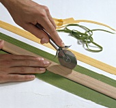 Hand cutting yellow and green pasta strips with pastry cutter and ruler