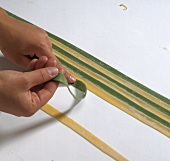 Hand combining yellow and green pasta strips on white background