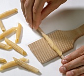 Hand rolling wrapped dough on rippled wood for preparing garganelli pasta, step 2