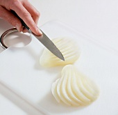 Peeled and halved pear being cut into slices on cutting board
