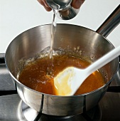 Water being poured in caramelized sugar in sauce pan