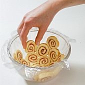 Hand arranging slices of roulade biscuit in bowl