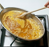 Hand stirring lime and orange juice with hot butter in pan