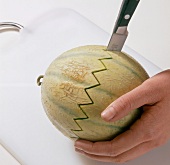 Melon being sliced in zigzag pattern with knife on cutting board