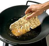 Noodles being added in oil for stir fry in wok, step 1