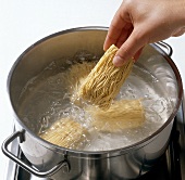 Noodles being added to boiling water while preparing bami goreng pasta, step 1