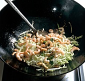 Shrimps and chopped cabbage being fried in wok while preparing bami goreng pasta. step 5