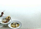 Two bowls of ravioli with beetroot and lamb filling on white background, copy space