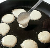 Blini batter being poured in small pancake size in hot pan