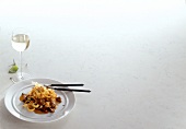 Tagliatelle with rabbit ragout on plate with wine glass on white background, copy space
