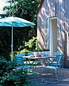 Terrasse vor Holzhaus mit gedecktem Tisch und blauen Stühlen, Schirm